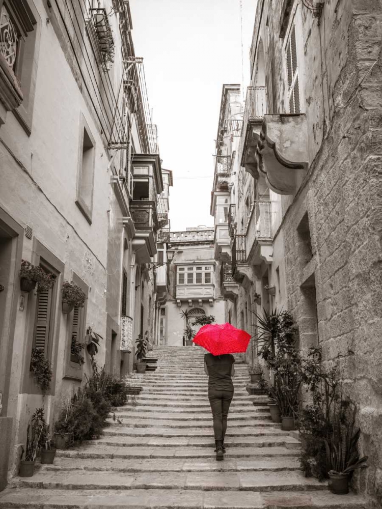 Tourist with umbrella in steps through houses in Birgu, Malta