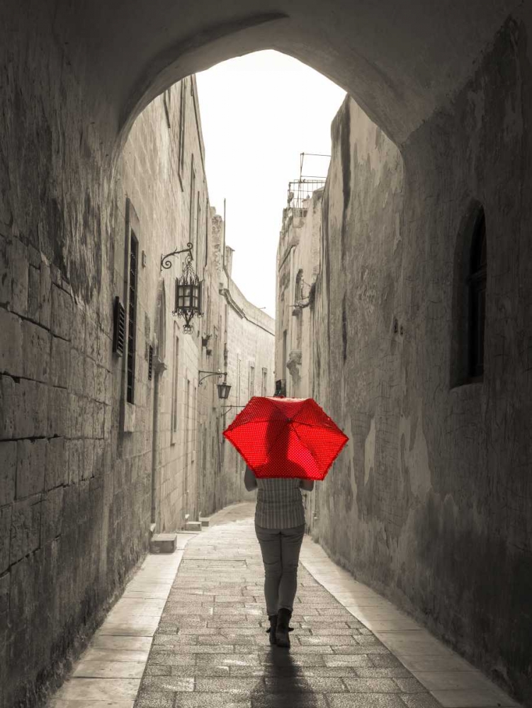 Tourist with umbrella walking through narrow street in Mdina, Malta