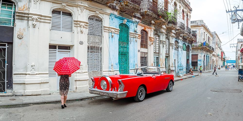 Woman with red umbrella by a vintage car on the street of Havana, Cuba, FTBR 1851