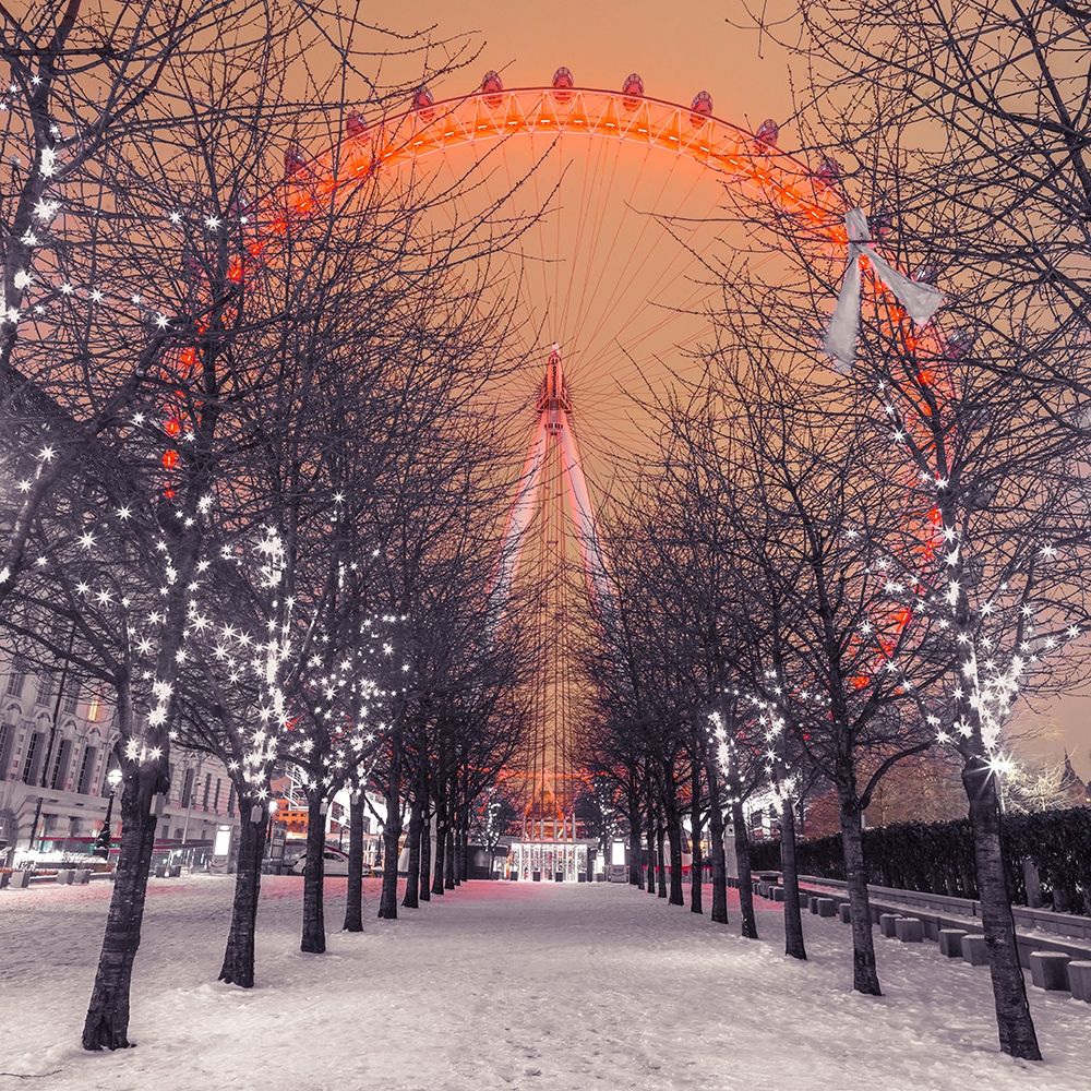 London Eye at night with trees in the foreground lit with lights and snow on the pathway-London-UK