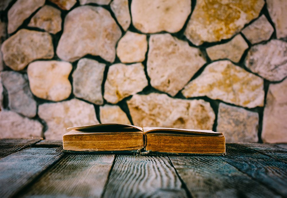 Old Open Book On Old Wooden Table On A Background Of Stone Walls
